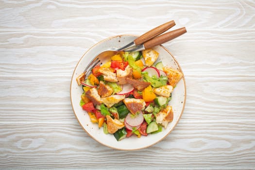 Traditional Levant dish Fattoush salad, Arab cuisine, with pita bread croutons, vegetables, herbs. Healthy Middle Eastern vegetarian salad, rustic wooden white background top view.