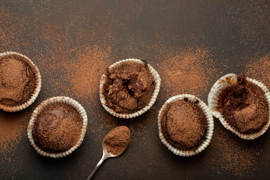 Chocolate browny muffins and cocoa in teaspoon top view on brown rustic stone background, sweet homemade dark chocolate cupcakes.