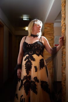 Full length view of a blonde female model, dressed in a black and white queen dress in dark corridor. Mysterious stranger alone inside castle or hotel