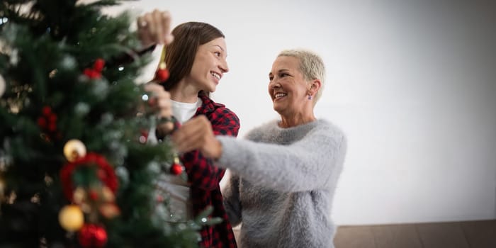 Family winter holiday and concept happy senior woman with adult daughter decorate christmas tree at home.