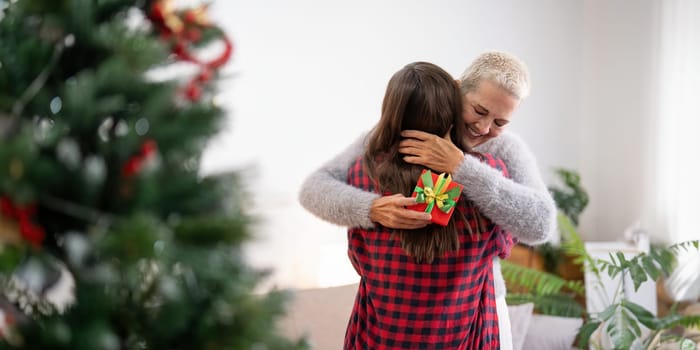 Daughter giving present to happy mother and embrace indoors at home at Christmas.