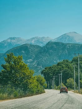 vertical photo, on the road through the mountains and forest, red car. car travel and summer holiday concept