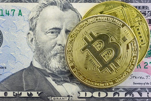 Bitcoin coins lie on a fifty dollar bill, close-up