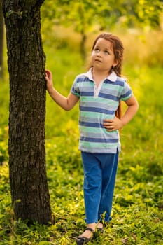 A child stands near a tree in the garden
