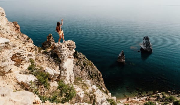 Woman travel sea. Happy tourist taking picture outdoors for memories. Woman traveler looks at the edge of the cliff on the sea bay of mountains, sharing travel adventure journey.