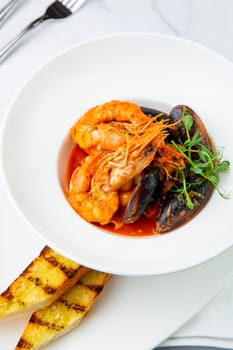 shrimp and mussels with herbs in a white plate with toasted bread