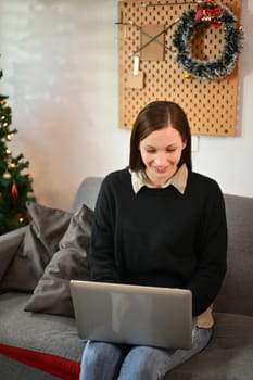 Happy young woman using laptop on sofa during Christmas holidays at home.