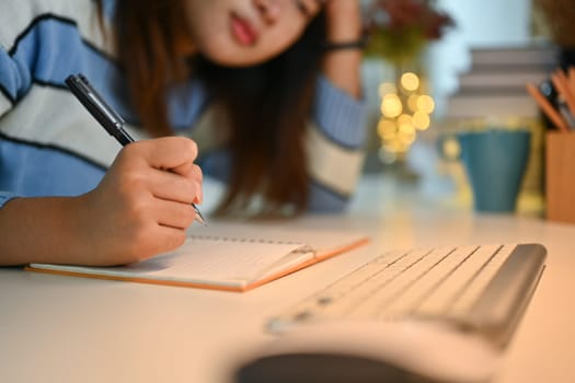 Bored asian woman sitting studying and doing homework a desk in living room.