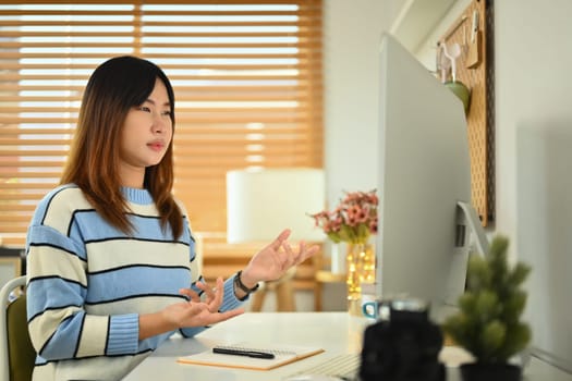 Photo of young Asian woman looking at computer monitor attending virtual online training at home.