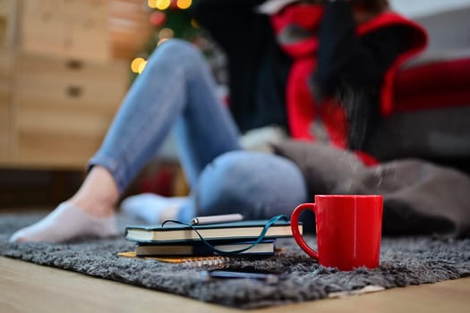 Cup of hot chocolate and books on carpet in a cozy living room. Christmas, winter and holidays concept.