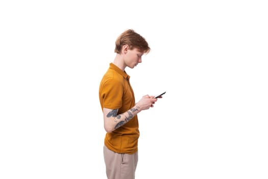 young stylish red-haired man with a haircut and a tattoo on his arm is dressed in a yellow t-shirt chatting on the phone.