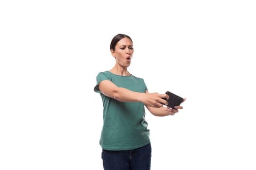 well-groomed young brunette woman dressed in a green t-shirt and jeans plays a game on the phone.
