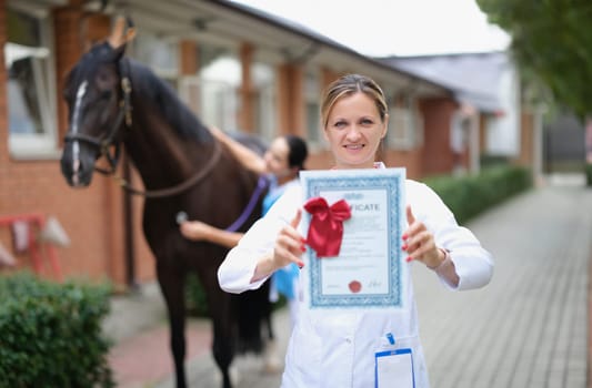 Woman veterinarian is holding medical certificate in background horse. Medical examination of horses concept