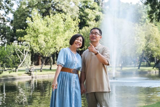 Senior man and wife holding a picnic basket walking among the green trees in the park A retired couple in their 60s walked through the garden together enjoying their vacation..