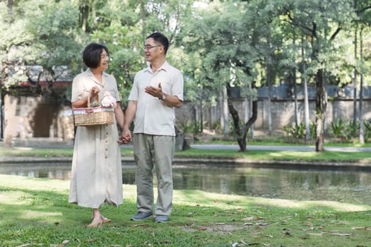 Senior man and wife holding a picnic basket walking among the green trees in the park A retired couple in their 60s walked through the garden together enjoying their vacation..