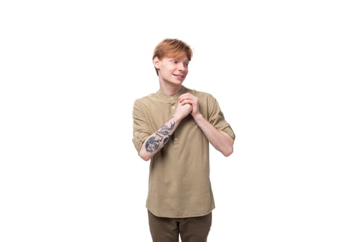 a young slender red-haired caucasian guy dressed in a khaki short-sleeve shirt holds his hands near his chest.