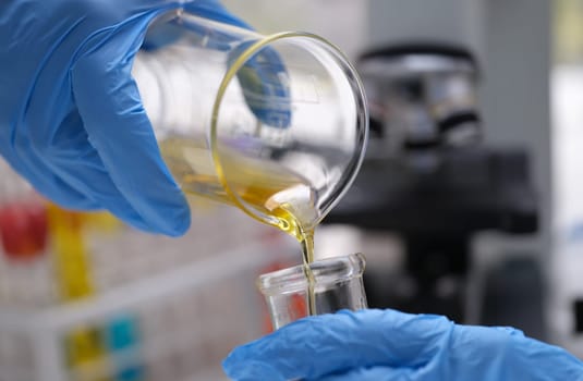 Chemical laboratory research and liquid oil processing. Scientist manually pouring yellow liquid from a chemical test tube into a glass flask concept