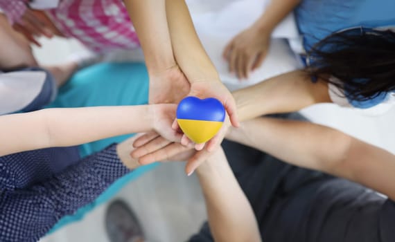 Group of people holding hearts with flag of Ukraine in their hands closeup top view. Worldwide support and assistance to Ukrainian people concept