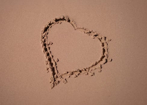 Heart is painted on sand of sea beach closeup. Honeymoon romantic trip concept