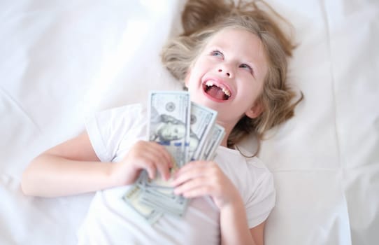 Little girl without front teeth holding money in her hands and smiling. Investment in pediatric dentistry concept