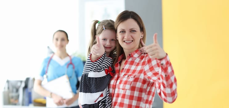 Little girl and mom showing thumb up at doctor appointment. Family medicine concept