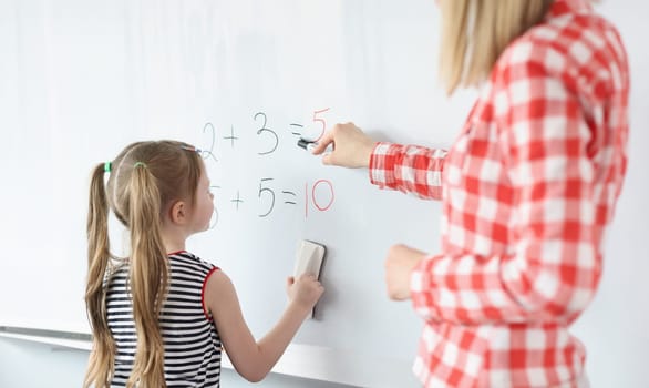 Little girl and teacher solving math equations on blackboard. Preschool education concept