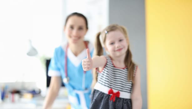 Little girl showing thumb up at doctor appointment closeup. Pediatrics concept