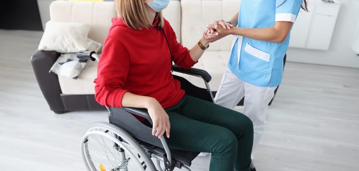 Therapist holding hand of disabled woman in protective medical mask closeup. Working with people with disabilities during covid19 pandemic concept
