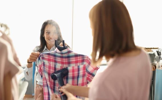 Woman ironing clothes with steamer in laundry. Clothing care services concept