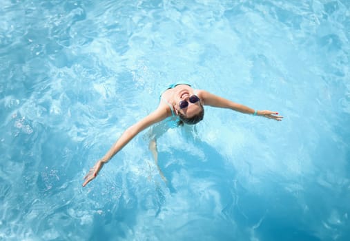 Young woman in sunglasses swimming in pool top view. Rest at resort concept