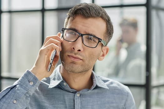 young man in a blue shirt talking on the phone in the office