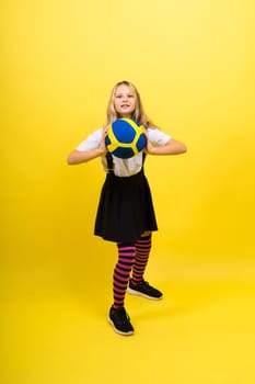 A teenager girl holds volleyball ball in hand and smiles on red yellow background. Studio photo.