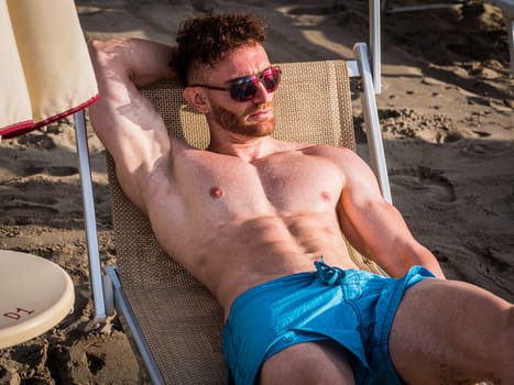 A shirtless man laying in a chair on the beach