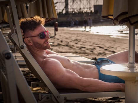 A shirtless man laying in a chair on the beach
