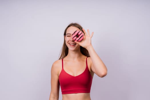 Lovely young caucasian woman in a sports wear with donuts on grey and yellow studio background.