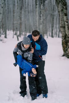 Dad hugging mom holding little baby upside down in winter forest. High quality photo