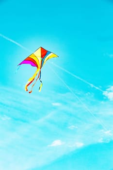 Rainbow kite flying in blue sky in sunny day in summer. Childhood concept.