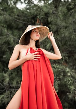 naked sexy woman in red fabric and Asian triangular hat on the background of nature