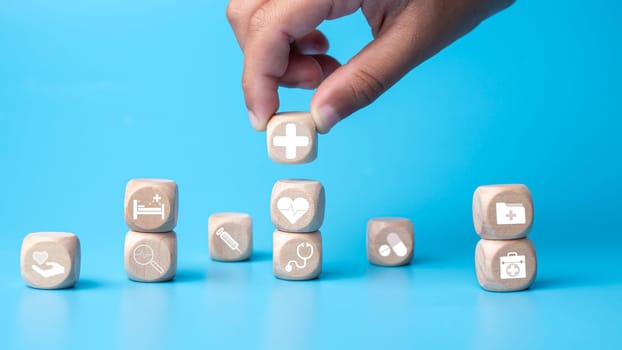 Concept of health insurance and medical. Human hold wooden block with icons about health insurance and access to health care, health care planning on a blue background.