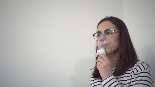 A young woman breathes through an inhaler mask closeup. A girl in glasses with an oxygen mask is being treated for a respiratory infection. 4k