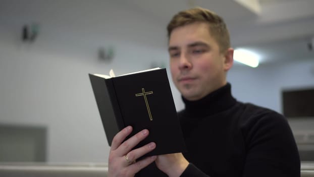 A young man reads the Bible while sitting on a church bench. A Protestant man reads the Bible in church. 4k