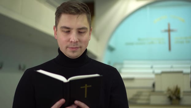 A young man reads the Bible against the backdrop of a cross in a church. A Protestant man stands reading the Bible in church. 4k