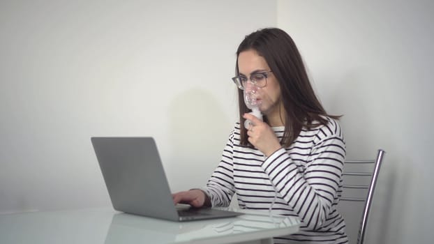 A young woman breathes through an inhaler and uses a laptop. A girl in glasses with an oxygen mask is being treated for a respiratory infection and typing on a netbook. 4k