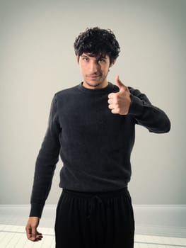 A man in a black sweater giving a thumbs up, in studio shot on neutral background