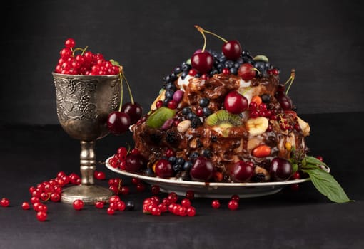 A luxurious cake with fruits and berries in a glass goblet on a dark background.