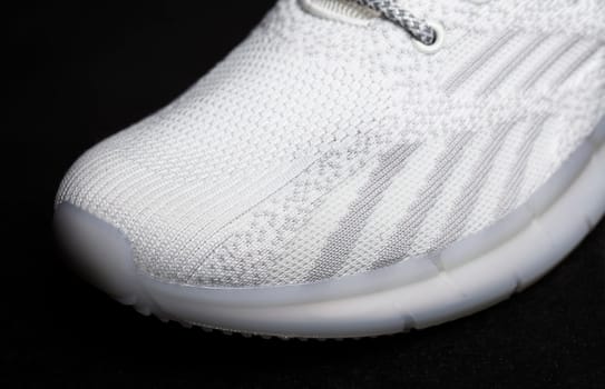 White fabric sneaker with embossed sole on a black background close-up.