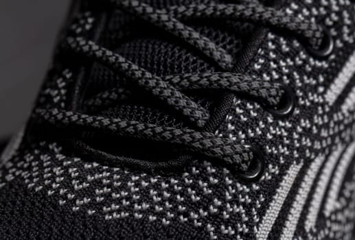 Part of a gray fabric sneaker with laces on a dark background.