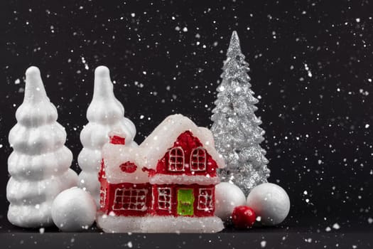 Festive snowy dark Christmas background. Red miniature house surrounded by white Christmas trees.