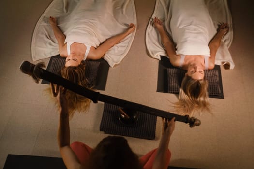 girls, lying on the floor, relax under the sound instrument of the rain staff in the fitness room.