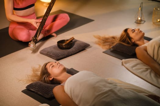 girls, lying on the floor, relax under the sound instrument of the rain staff in the fitness room.